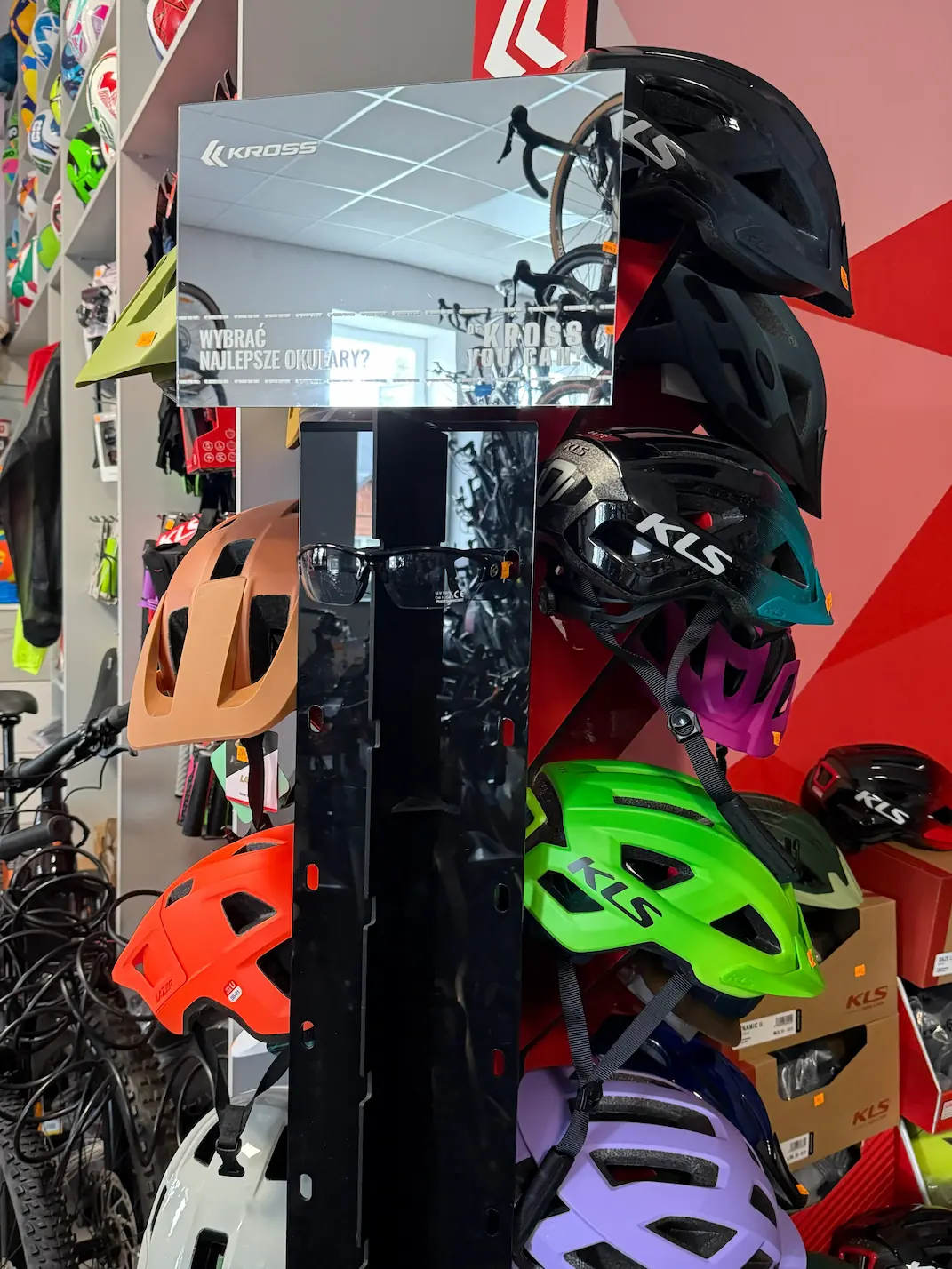 Stojak z kaskami rowerowymi oraz sportowymi okularami przeciwsłonecznymi w sklepie rowerowym Brylant Tuchów.